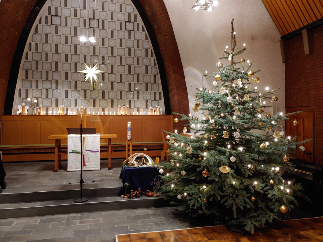 Kirche mit Krippe im Altarraum und Christbaum davor. Kerzen und Engelsfiguren im Hintergrund.
