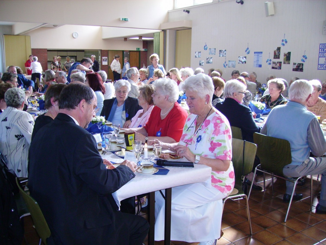 Menschen an langen Tischtafeln im großen Saal